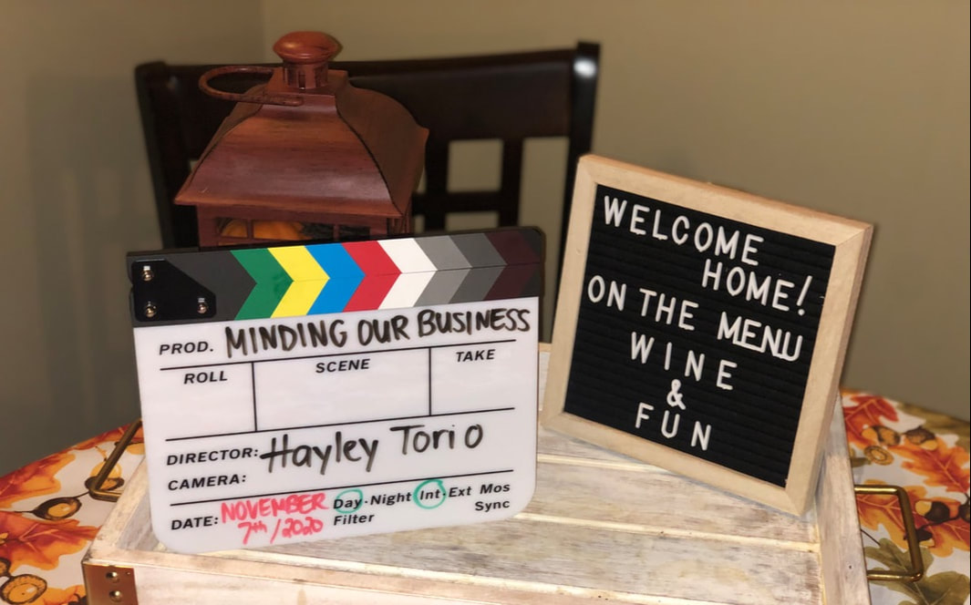 Minding our Business movie slate next to sign that reads, 