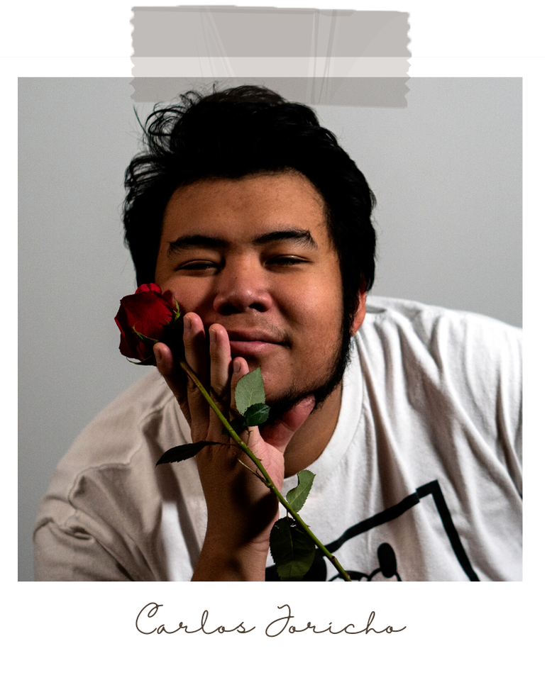 Carlos Joricho rests his face against his hand, while holding a rose. He is looking at the camera.
