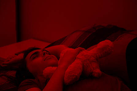 Evelyn is laying down listening to music to fell more comfortable fronting, red hue light filters the picture